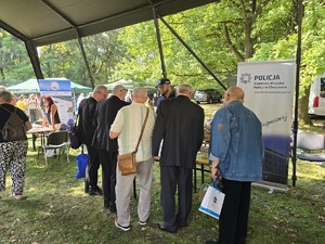 Na zdjęciu policjant przy stosiku profilaktycznym a za nim baner Komendy Miejskiej Policji w Chorzowie oraz 5 mężczyzn stojących przed stoiskiem
